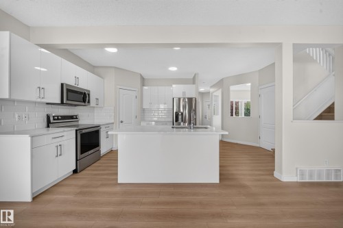 Modern kitchen with white shaker-style cabinetry, stainless steel appliances, a center island, and wood-finish flooring - 7836 7 Ave Sw Sw, Edmonton, AB 