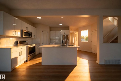Modern kitchen featuring white cabinetry, stainless steel appliances, a center island, and wood-finish flooring - 7836 7 Ave Sw Sw, Edmonton, AB 
