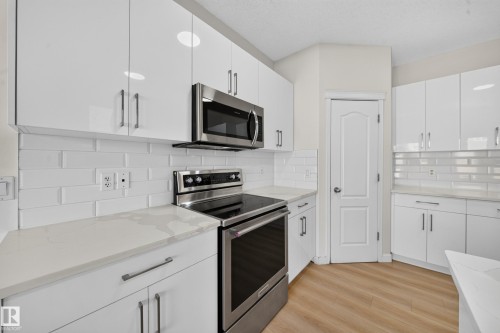 Contemporary kitchen featuring white cabinetry, stainless steel appliances, white subway tile backsplash, light-toned wood-finish flooring, and light countertops - 7836 7 Ave Sw Sw, Edmonton, AB 