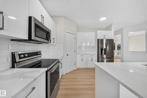White cabinetry, stainless steel appliances, white subway tile backsplash, wood-finish flooring, and white countertops - 7836 7 Ave Sw Sw, Edmonton, AB 