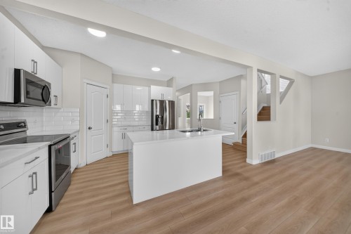 Kitchen featuring white cabinetry, stainless steel appliances, quartz countertops, a center island with sink, and wood-finish flooring - 7836 7 Ave Sw Sw, Edmonton, AB 