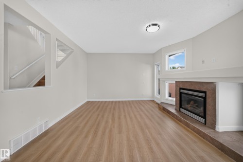 Expansive living area featuring wood-finish flooring and a tiled fireplace - 7836 7 Ave Sw Sw, Edmonton, AB 