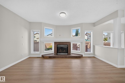 Wood-finish flooring, central fireplace with dark stone hearth, surround, and mantle, multiple windows, and a recessed ceiling light fixture - 7836 7 Ave Sw Sw, Edmonton, AB 