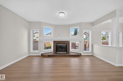 Wood-finish flooring, central fireplace with dark stone hearth, surround, and mantle, multiple windows, and a recessed ceiling light fixture - 