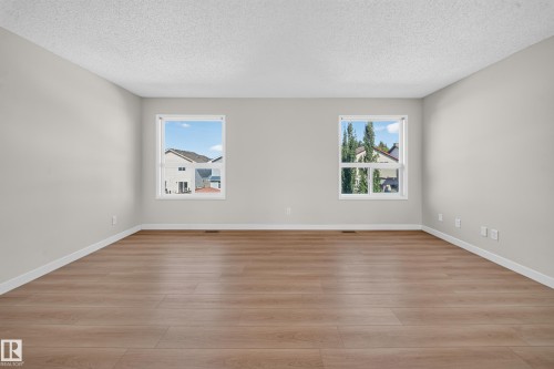 Spacious room featuring light wood-finish flooring, two large windows, white trim, and light gray walls - 7836 7 Ave Sw Sw, Edmonton, AB 