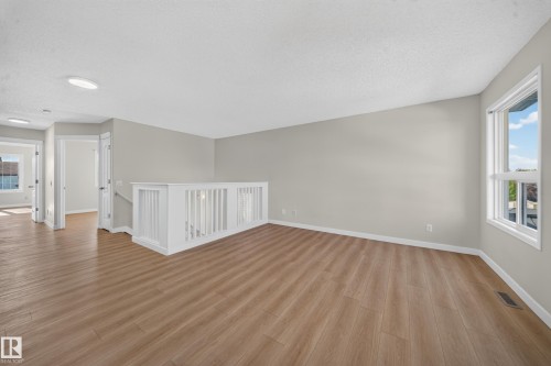 Open concept upper level featuring wood-finish flooring, neutral wall tones, and a white spindle railing - 7836 7 Ave Sw Sw, Edmonton, AB 