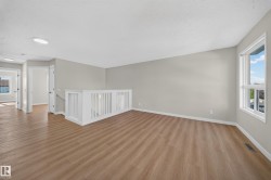 Open concept upper level featuring wood-finish flooring, neutral wall tones, and a white spindle railing - 