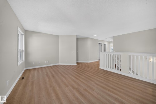Open-concept area featuring wood-finish flooring, light-toned walls, a white window frame, and a white baluster railing - 7836 7 Ave Sw Sw, Edmonton, AB 
