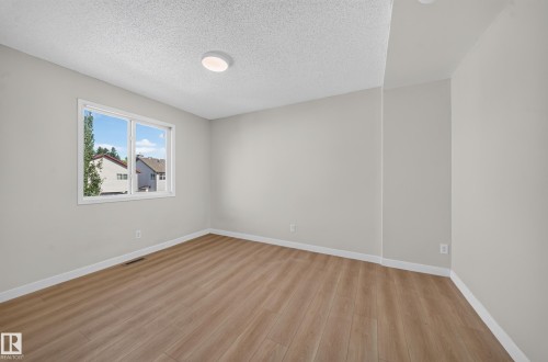 Bright room featuring wood-finish flooring, a large window, a flush-mount ceiling light, and light-toned walls - 7836 7 Ave Sw Sw, Edmonton, AB 