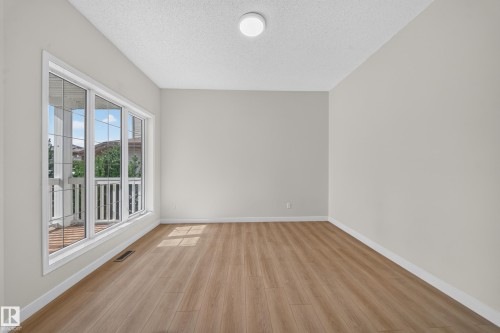 Spacious room featuring light wood-finish flooring, neutral wall paint, and a large multi-pane window - 7836 7 Ave Sw Sw, Edmonton, AB 