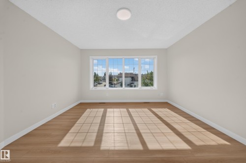 Expansive room featuring a large multi-pane window, wood-finish flooring, and a flush-mount ceiling light fixture - 7836 7 Ave Sw Sw, Edmonton, AB 