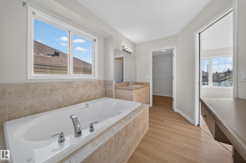 Soaking tub with tiled surround, wood-finish flooring, single vanity with integrated sink, and built-in closet with wire shelving - 7836 7 Ave Sw Sw, Edmonton, AB 