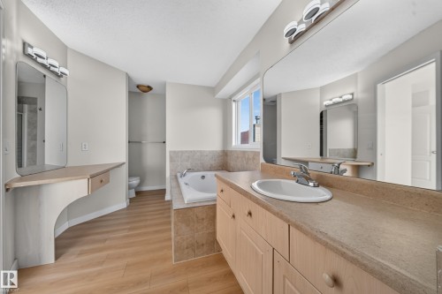 Dual vanity with integrated sinks, recessed bathtub, wood-finish flooring, built-in makeup vanity, and large wall-mounted mirrors - 7836 7 Ave Sw Sw, Edmonton, AB 
