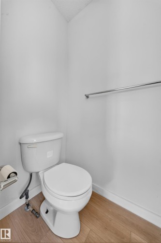 White toilet with wood-finish flooring and a chrome towel bar - 7836 7 Ave Sw Sw, Edmonton, AB 