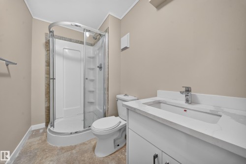Corner shower with a curved glass enclosure, white vanity with an integrated sink, chrome faucet, and neutral-toned walls - 7836 7 Ave Sw Sw, Edmonton, AB 