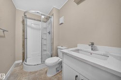 Corner shower with a curved glass enclosure, white vanity with an integrated sink, chrome faucet, and neutral-toned walls - 