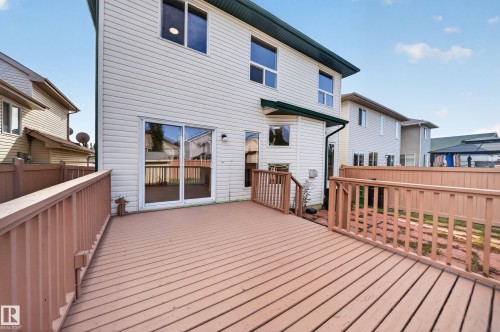 Expansive wood-finish deck with railing, sliding glass door access, and exterior wall lighting - 7836 7 Ave Sw Sw, Edmonton, AB 