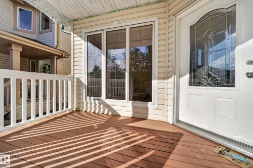 Front porch with wood-finish decking, white railings, and vinyl siding - 7836 7 Ave Sw Sw, Edmonton, AB 