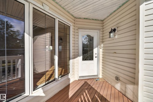 Covered entry with wood-finish decking, white siding, and a decorative glass front door - 7836 7 Ave Sw Sw, Edmonton, AB 