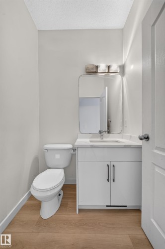 White vanity with a single basin sink, contemporary rectangular mirror, and three-light wall fixture - 7836 7 Ave Sw Sw, Edmonton, AB 