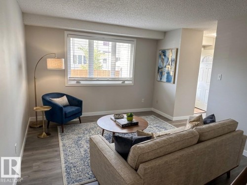 Wood-finish flooring throughout, complemented by a large window with blinds and white trim - 9G Clareview Village Nw, Edmonton, AB 