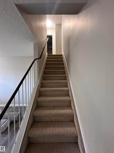 Staircase featuring textured carpet, white risers, and a metal railing - 9G Clareview Village Nw, Edmonton, AB 