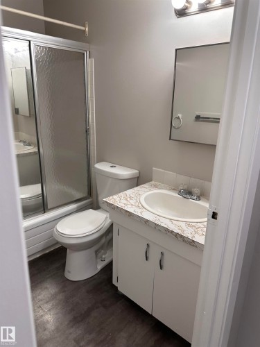 Bathroom featuring a shower enclosure with sliding glass doors, a white toilet, a vanity with a laminate countertop, and wood-finish flooring - 9G Clareview Village Nw, Edmonton, AB 