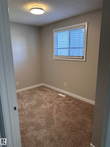 Room featuring neutral-toned walls, textured carpeting, a window with blinds, and a flush-mount ceiling light - 9G Clareview Village Nw, Edmonton, AB 