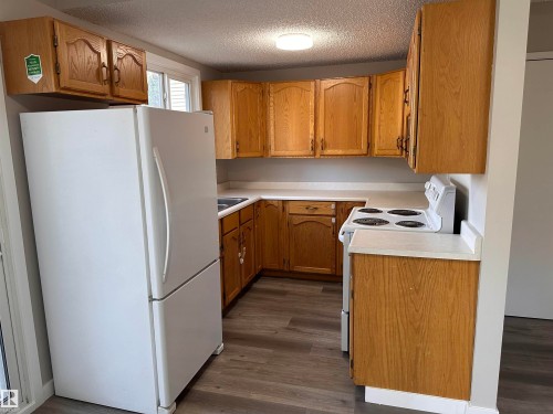 Kitchen featuring wood-finish cabinetry, light-toned countertops, and durable wood-look flooring - 9G Clareview Village Nw, Edmonton, AB 