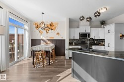 Modern kitchen featuring white cabinetry, stainless steel appliances, a dark stone countertop, and a center island with an integrated sink - 