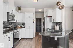 Contemporary kitchen featuring white cabinetry, stainless steel appliances, dark countertops, and wood-finish flooring - 