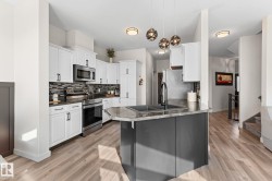 Kitchen featuring white cabinetry, stainless steel appliances, a dark backsplash, a kitchen island with a double basin sink, and wood-finish flooring - 
