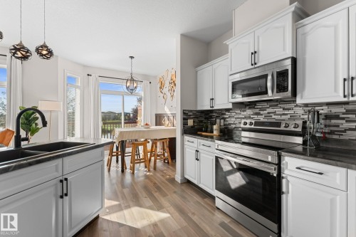 White cabinetry with black hardware, stainless steel appliances, dark countertops, a tiled backsplash, and wood-finish flooring - #5 4900 62 St, Beaumont, AB 