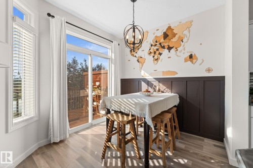 Wood-finish flooring, sliding glass doors to exterior, dark wainscoting, and a decorative orb chandelier - #5 4900 62 St, Beaumont, AB 