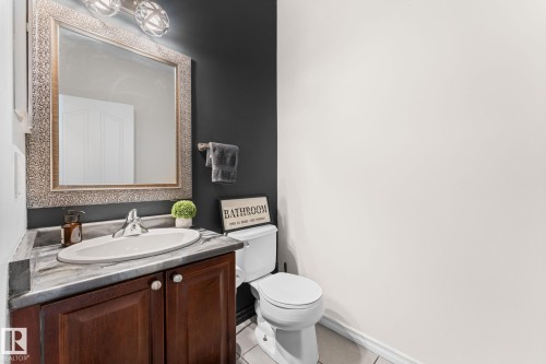 Powder room featuring a single vanity with wood-finish cabinetry, a white oval sink, and a framed mirror with integrated lighting - #5 4900 62 St, Beaumont, AB 