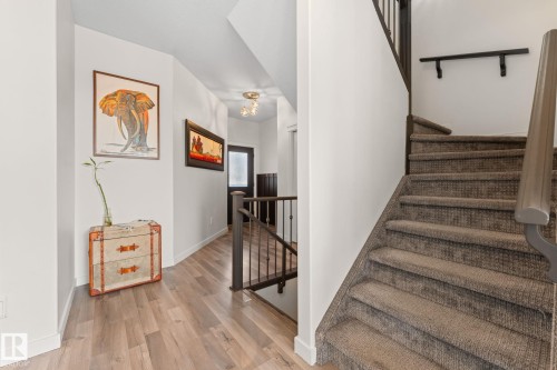 Wood-finish flooring, staircase with carpeted treads, dark wood railing, and a modern ceiling fixture - #5 4900 62 St, Beaumont, AB 