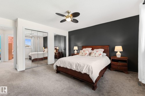 Carpeted bedroom featuring a ceiling fan, a dark accent wall, and mirrored sliding closet doors - #5 4900 62 St, Beaumont, AB 