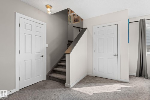 Carpeted staircase with dark wood-finish handrail, white panel doors, and neutral wall paint - #5 4900 62 St, Beaumont, AB 