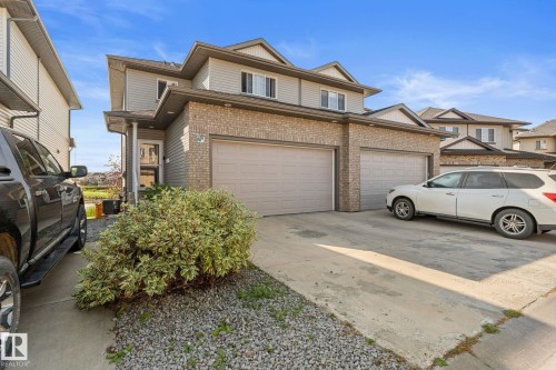 Exterior featuring brick and siding finishes, two attached garage doors, concrete driveway, and established landscaping - #5 4900 62 St, Beaumont, AB 