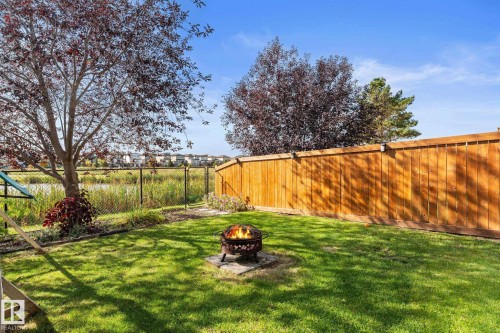 Grassed backyard featuring a wood fence, mature trees, and a chain-link fence bordering a pond - #5 4900 62 St, Beaumont, AB 