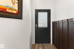 Dark wood-finish flooring, dark paneled wainscoting, and a black paneled door with a decorative glass insert - 