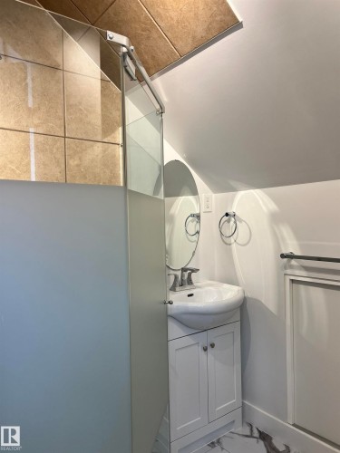 White vanity with two cabinet doors, ceramic vessel sink, wall-mounted oval mirror, and a glass shower enclosure with tiled walls - 11908 131 Street Nw, Edmonton, AB 