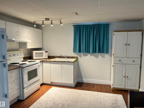 Kitchenette featuring white cabinetry, a built-in sink, white appliances, and wood-finish flooring - 11908 131 Street Nw, Edmonton, AB 