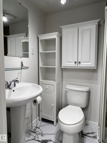 Pedestal sink with chrome-finish faucet, white toilet, white wall-mounted cabinet, and built-in shelving unit - 11908 131 Street Nw, Edmonton, AB 