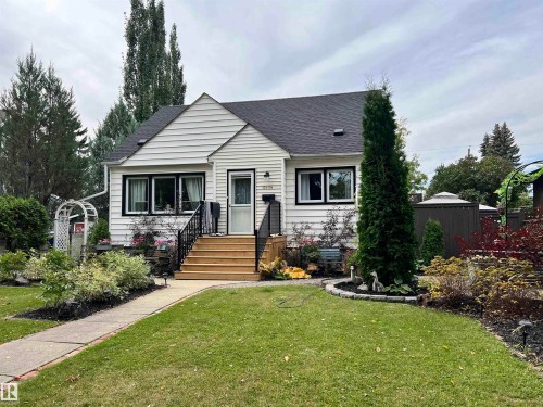 White siding exterior with black trim windows, a dark shingle roof, and a mature landscaped front yard - 11908 131 Street Nw, Edmonton, AB 
