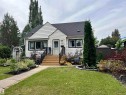 White siding exterior with black trim windows, a dark shingle roof, and a mature landscaped front yard - 11908 131 Street Nw, Edmonton, AB 