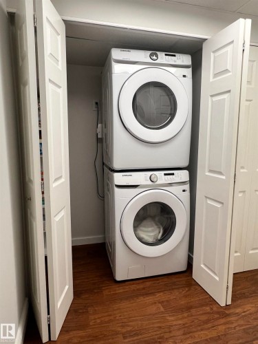 Built-in laundry closet with bi-fold doors, stacked white appliances, and wood-finish flooring - 11908 131 Street Nw, Edmonton, AB 