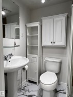 Pedestal sink with chrome-finish faucet, white toilet, white wall-mounted cabinet, and built-in shelving unit - 
