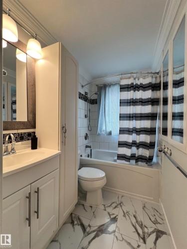 White vanity with integrated sink, modern wall sconces, white porcelain tile flooring with dark veining, built-in tub with white subway tile surround, and white storage cabinetry - 11908 131 Street Nw, Edmonton, AB 