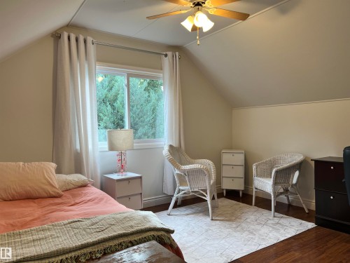 Sloped ceiling room featuring wood-finish flooring, a ceiling fan with integrated lighting, and a window with white trim - 11908 131 Street Nw, Edmonton, AB 